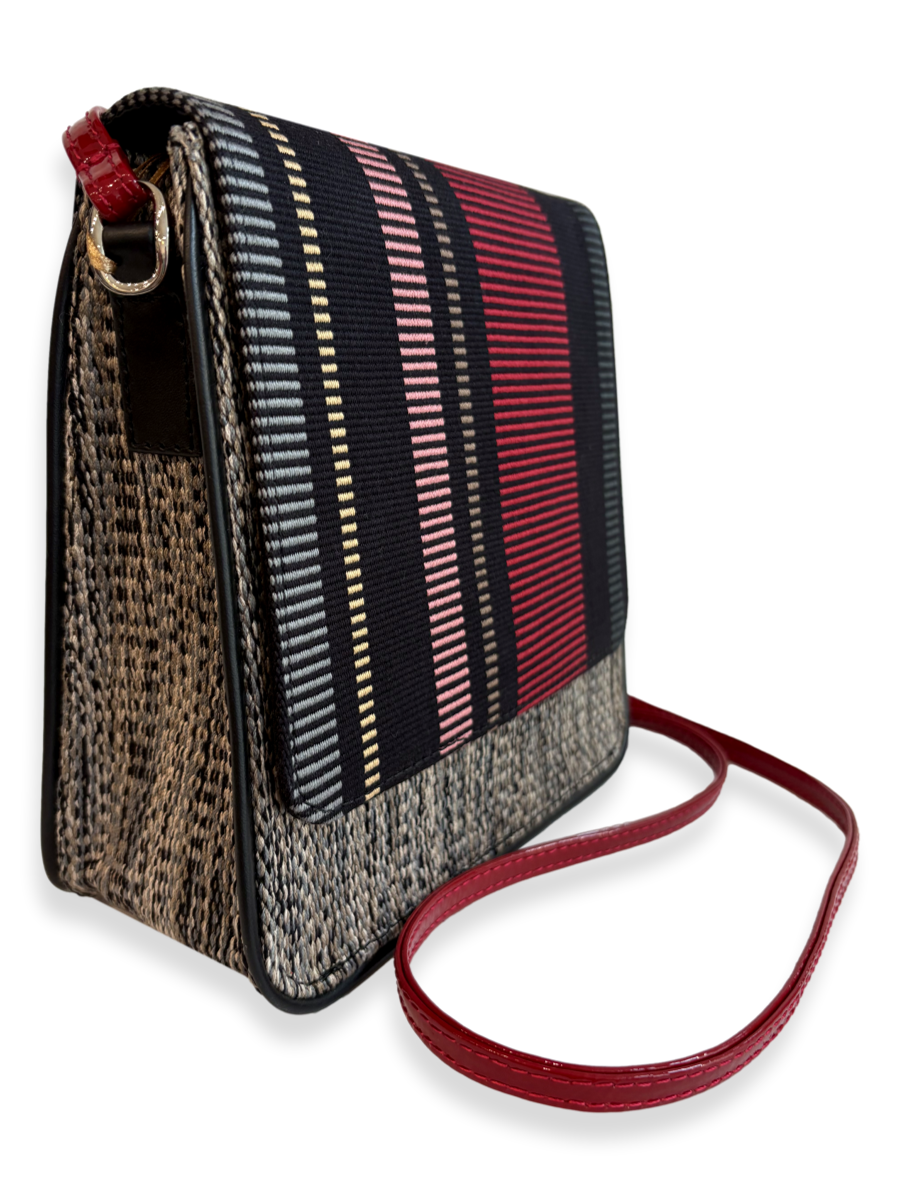 A rectangular shoulder bag with a woven patterned body, featuring a striped front flap in black, red, pink, and beige, with a red leather strap and gold-tone hardware, shown on a white background.