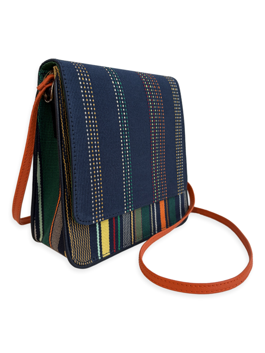 Angled view of the Cocktail designer crossbody handbag showcasing navy woven mercerized Pima cotton, orange pebbled leather strap, structured silhouette, and handcrafted Peruvian design.