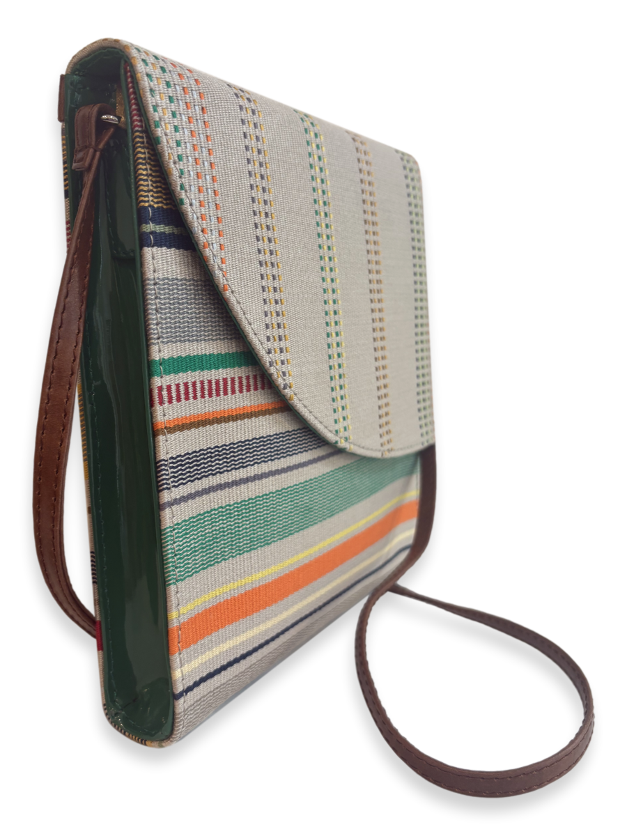 Angled view of the Curva one-of-a-kind designer crossbody bag showcasing premium Peruvian Pima cotton, smooth tan leather strap, glossy green leather sides, and a slim contemporary silhouette.