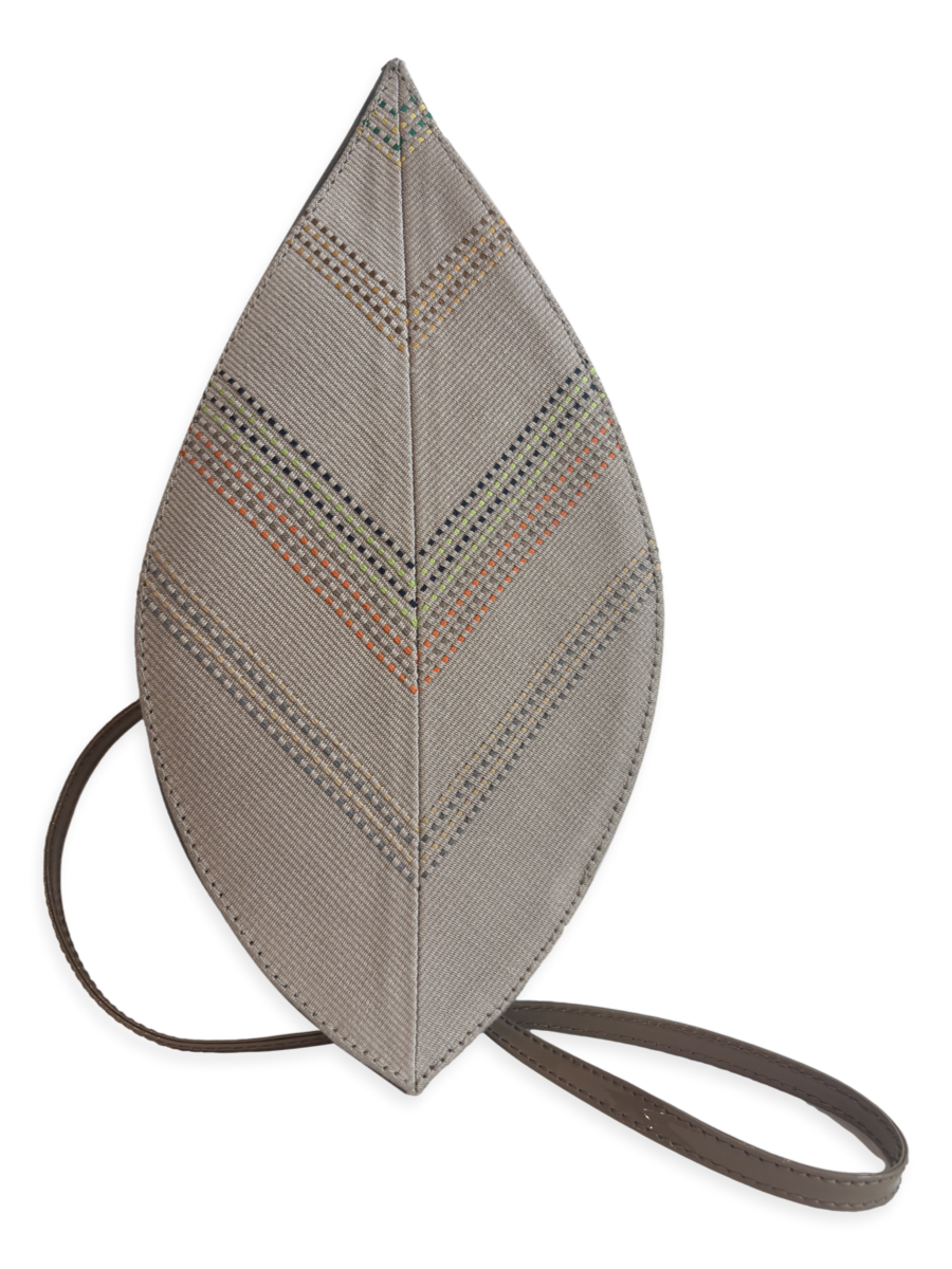 A leaf-shaped shoulder bag in textured taupe fabric with geometric chevron stitching in black, orange, and green, featuring a dark brown leather strap.