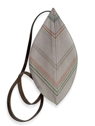 A leaf-shaped shoulder bag with a textured gray fabric body featuring geometric multicolor embroidered patterns, and a dark brown leather strap. Qinti the Peruvian Shop.
